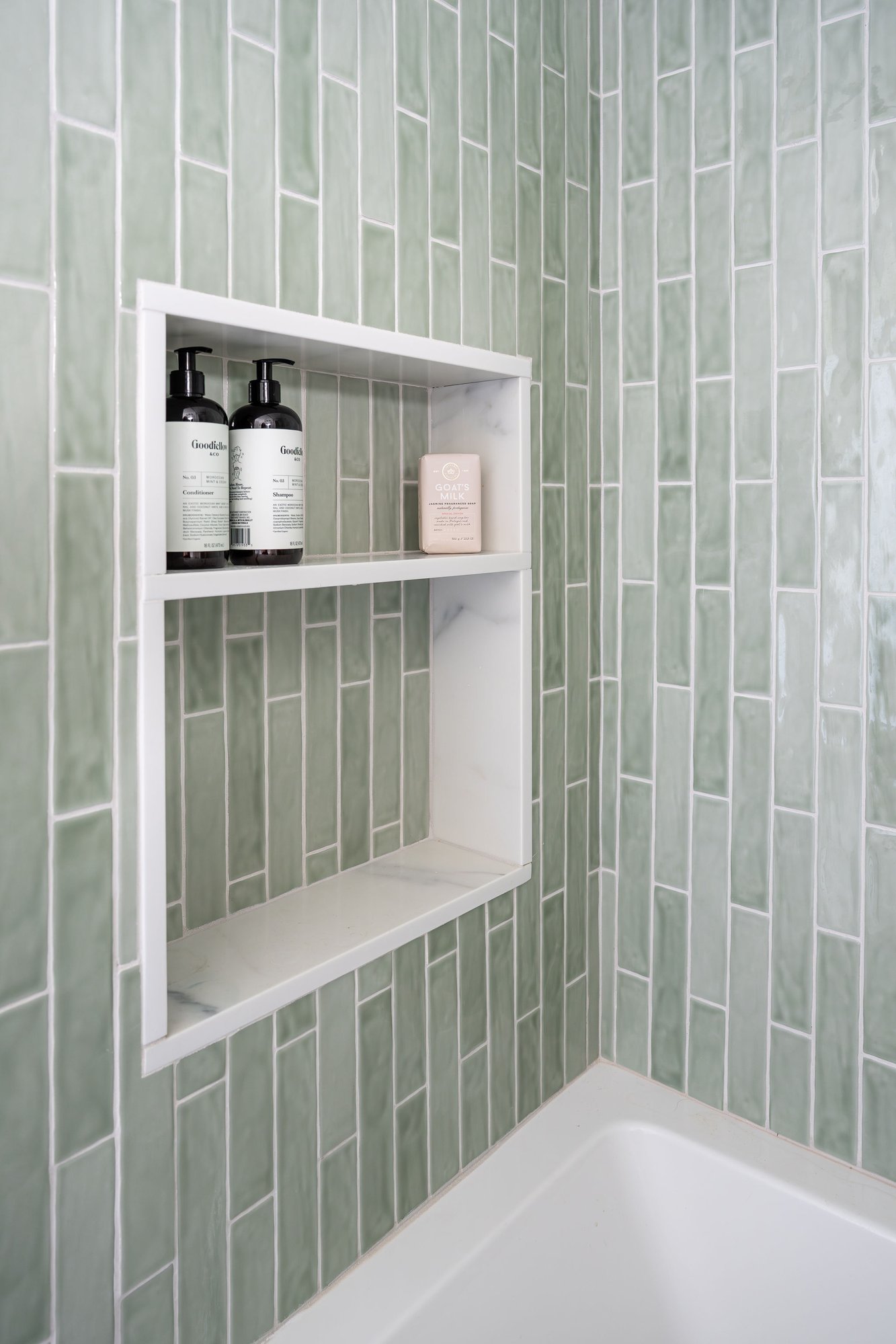 Built-in marble shower niche set within glossy sage-green vertical tile. Built-in marble shower niche set within glossy sage-green vertical tile.