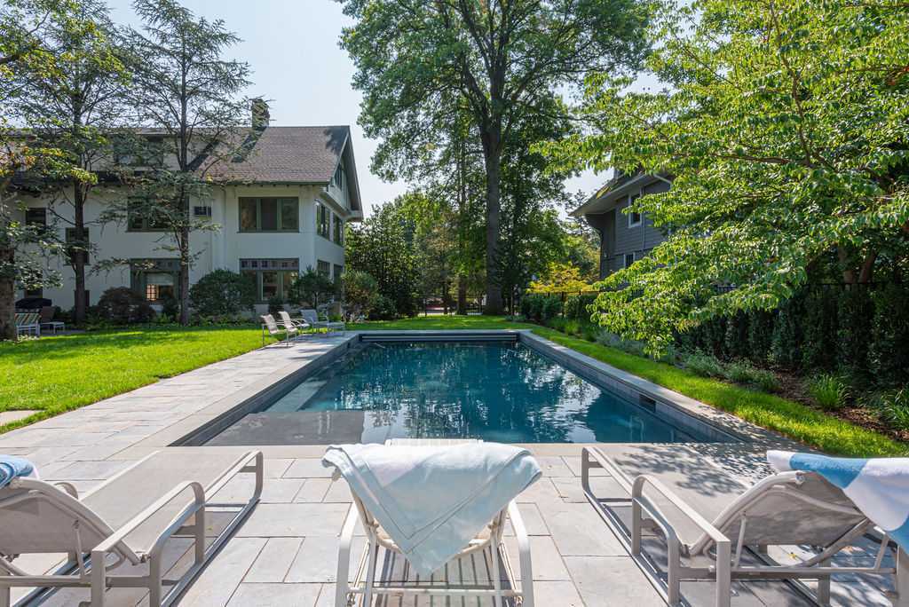 Custom in-ground pool surrounded by trees and stone pavers in Maplewood, NJ by G&L and Sons Renovations
