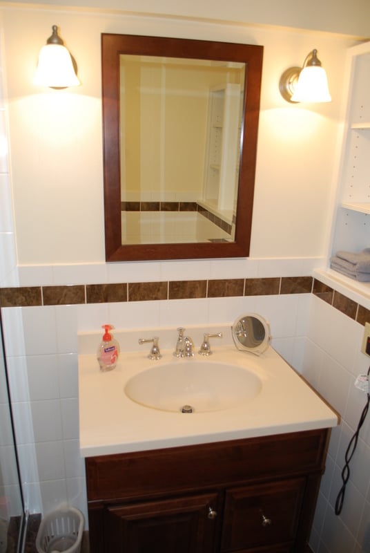 Basement bathroom vanity with dark wood cabinet and framed mirror by G&L and Sons Renovations in Woodland Park, NJ