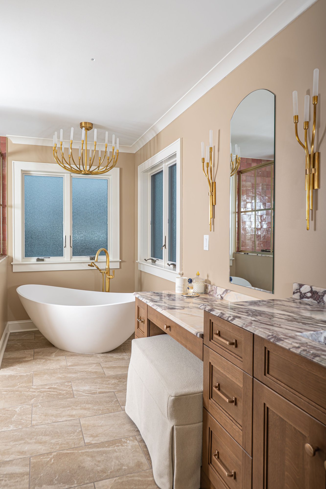 Remodeled bathroom with a freestanding white tub facing a wood vanity with a marble countertop and brass fixtures.