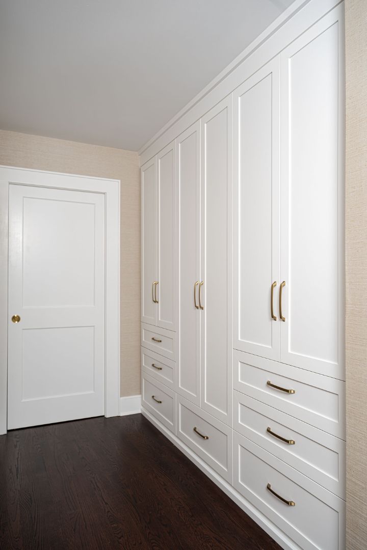 walk-in closet storage with white cabinets and brass hardware in a house remodeled by G&amp;L and Sons Renovations in Montclair, NJ.