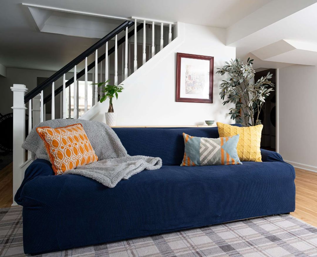 Colorful living room with navy couch, geometric pillows, and a staircase with black-and-white railings. | G&L and Sons Renovations