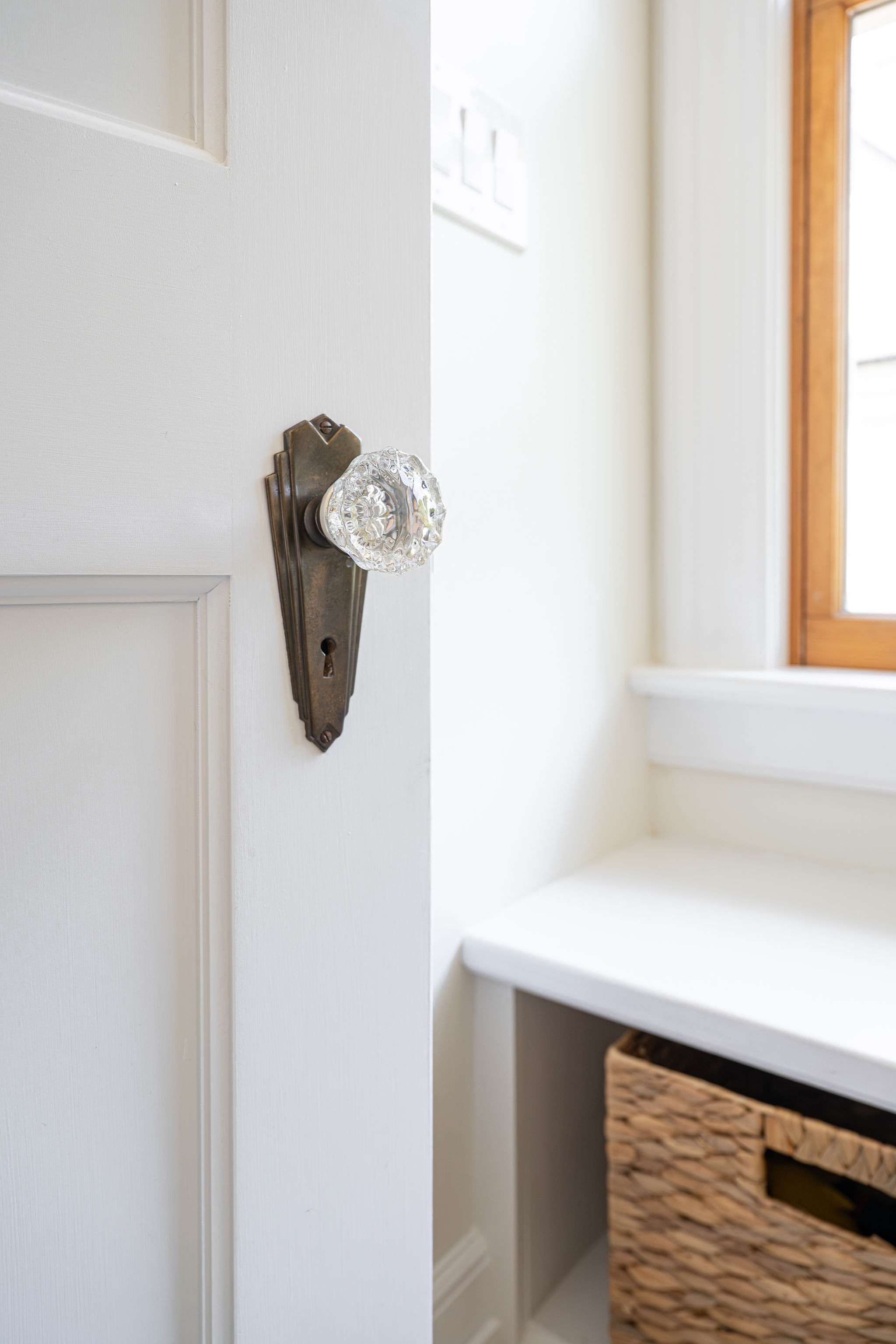 Close-up of a vintage glass doorknob and antique brass backplate beside a bright built-in bathroom storage nook.