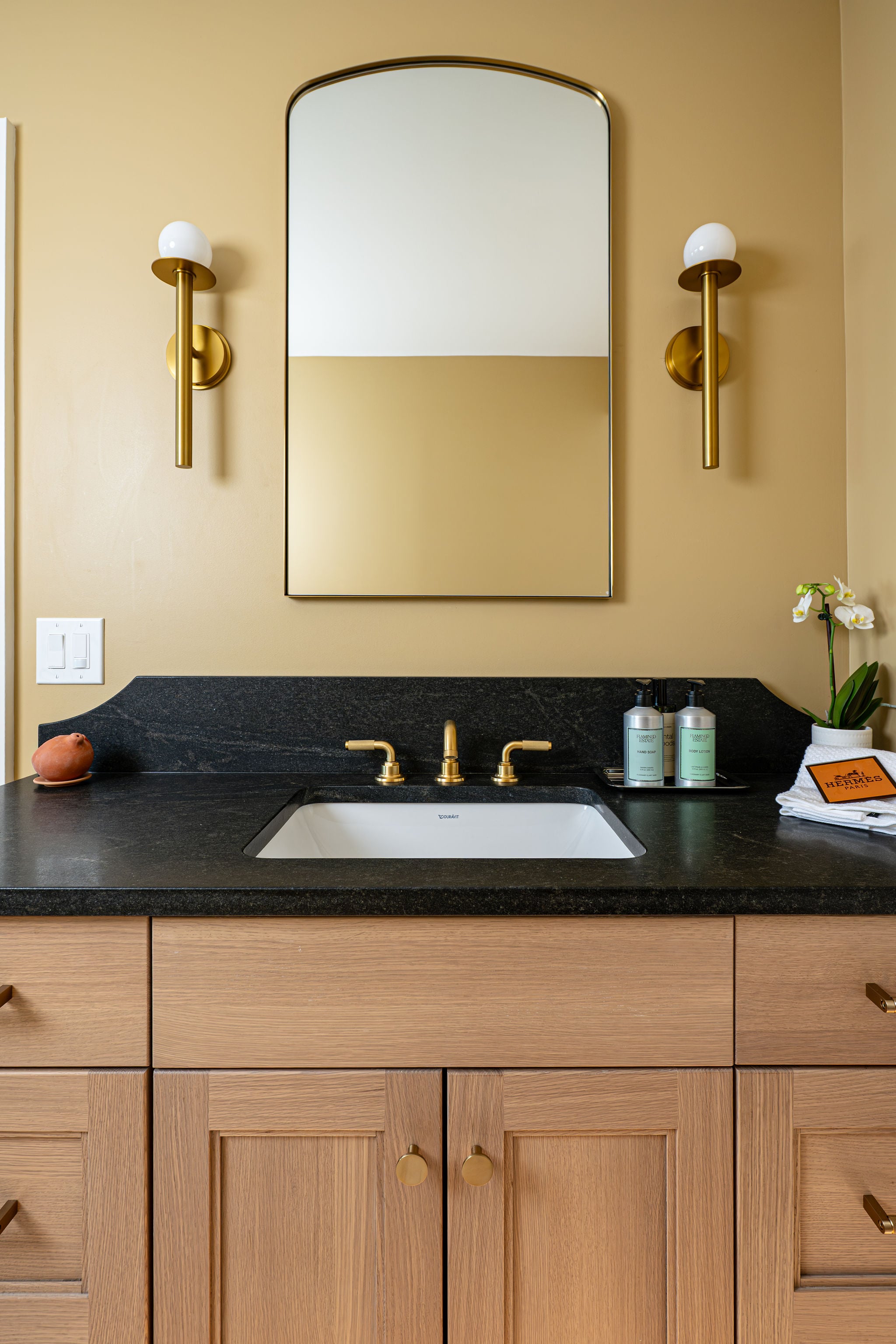 Image of a custom bathroom in Bergen County, New Jersey, with a black, landscape granite counter and brass fixtures.