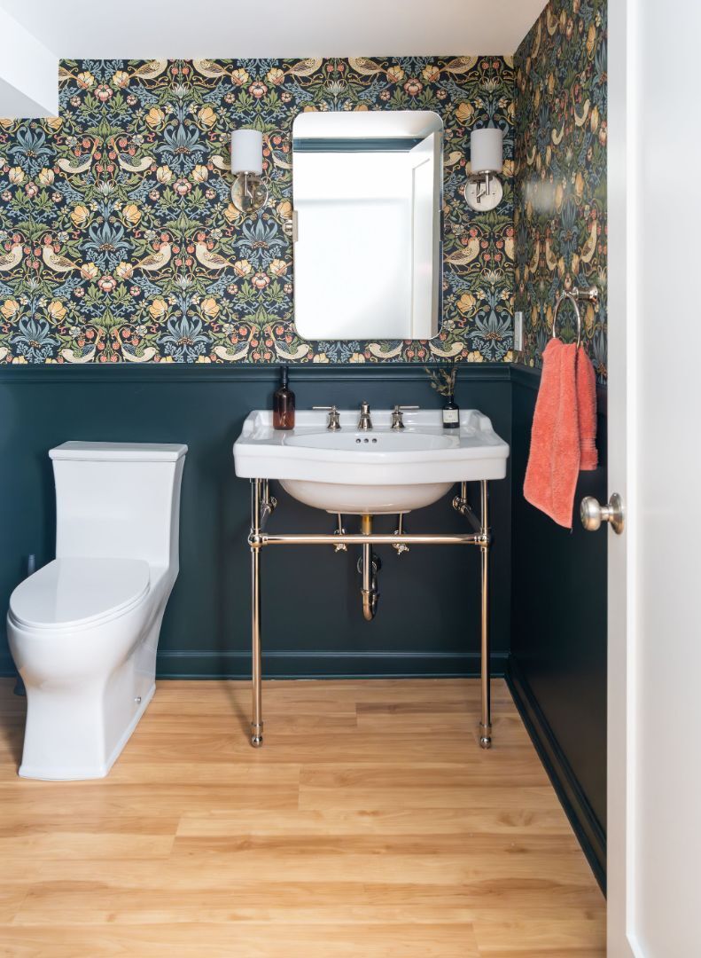 Eclectic powder room with dark green wainscoting, bold bird-and-floral wallpaper, and a vintage-style pedestal sink. | G&L and Sons Renovations